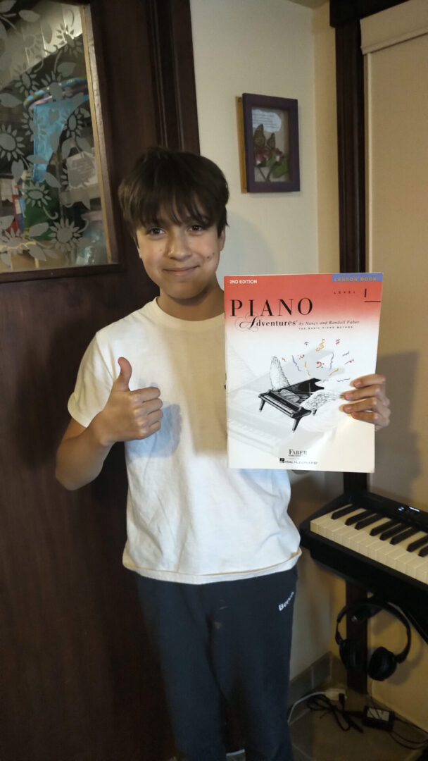 A young boy holding up a book about piano.